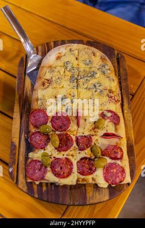 Langgestreckte argentinische Pizza mit Salami, Oliven und Käse Stockfoto