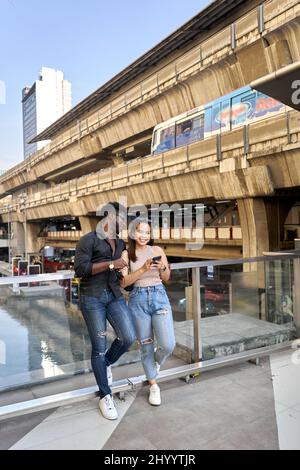 Freunde verschiedener Ethnien stehen in einem Einkaufszentrum, während sie ein Handy benutzen Stockfoto