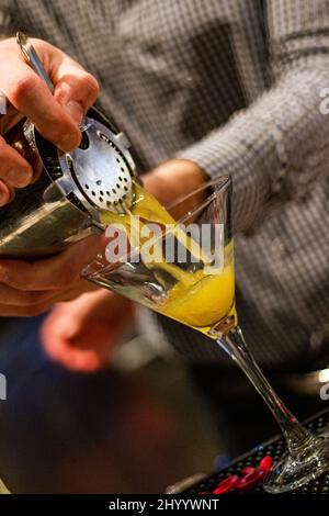 Vertikale Aufnahme des Barkeeps, der einen orangefarbenen Mango martini-Cocktail in das Glas gießt Stockfoto
