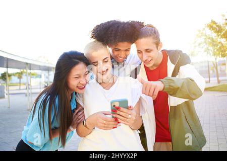 Eine Gruppe von glücklichen Freunden, die telefonieren und Spaß auf der Straße haben. Jugendliche teilen sich mit mobilen Zellen in Videoanrufen Stockfoto