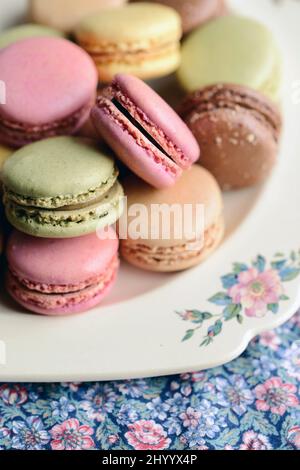 Französische Macarons auf einem Vintage-Teller auf einer floralen Tischdecke in natürlichem Licht Stockfoto