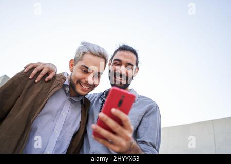 Homosexueller Mann paar zusammen mit Handys. Fröhliche Schwule, die etwas auf mobile Zelle schauen. Stockfoto