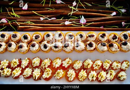 Canapé-Tassen mit Hühnersalat und getrockneten Aprikosen mit Boursin-Käse für Cocktailparty auf Tablett mit Zimtstangen und Blütenblättern verziert. Stockfoto