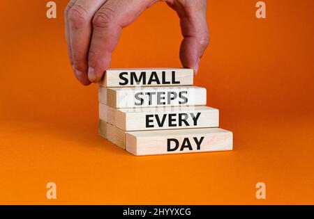 Symbol für kleine Schritte pro Tag. Konzept Worte kleine Schritte jeden Tag auf Holzblöcken. Geschäftsmann Hand. Schöne orange Tisch orange Hintergrund. Klein Stockfoto