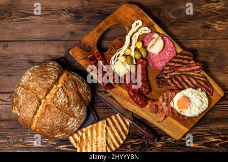 Verschiedene Arten von gegrillten Würstchen mit Ei. Eine Auswahl an gegrilltem Gourmet-Fleisch auf einem rustikalen Holzbrett. Gegrillte Würstchen mit hausgemachtem Brot. Stockfoto