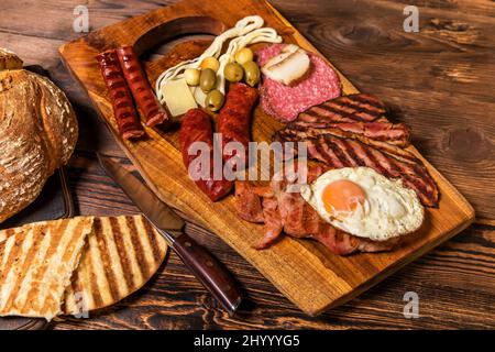 Verschiedene Arten von gegrillten Würstchen mit Ei. Eine Auswahl an gegrilltem Gourmet-Fleisch auf einem rustikalen Holzbrett. Gegrillte Würstchen mit hausgemachtem Brot. Stockfoto