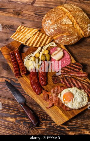 Verschiedene Arten von gegrillten Würstchen mit Ei. Eine Auswahl an gegrilltem Gourmet-Fleisch auf einem rustikalen Holzbrett. Gegrillte Würstchen mit hausgemachtem Brot. Stockfoto