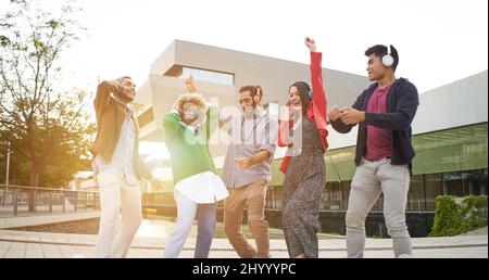 Eine Gruppe von glücklichen Menschen im Freien, die mit Kopfhörern im Freien feiern und tanzen. Stockfoto