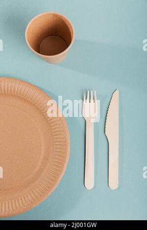 Einweggeschirr aus Papier. Tassen, Teller, Holzgabeln und Messer auf blauem Hintergrund. Kunststofffreies und abfallfreies Konzept. Stockfoto