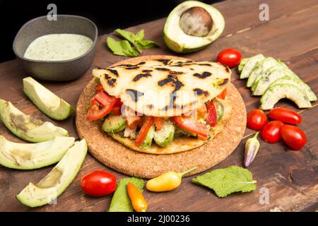 Arepas - traditionelle kolumbianische Küche ursprünglich aus Lateinamerika auf einem alten rustikalen Holztisch mit Fleisch, Gemüse und Avocado gemischt angeordnet Stockfoto