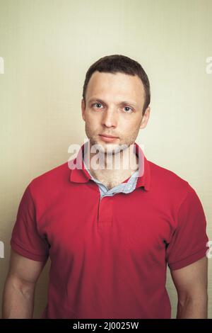 Studioporträt junger Erwachsener europäischer Mann in rotem Poloshirt Stockfoto