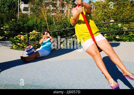 Ein junges Mädchen posiert für ihre Mutter auf einer Seilschaukel auf einem Spielplatz Stockfoto