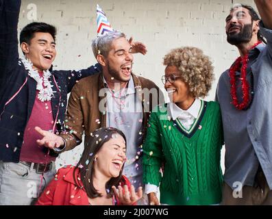 Junge Menschen blasen Konfetti aus den Händen. Freunde feiern Geburtstag im Freien. Stockfoto