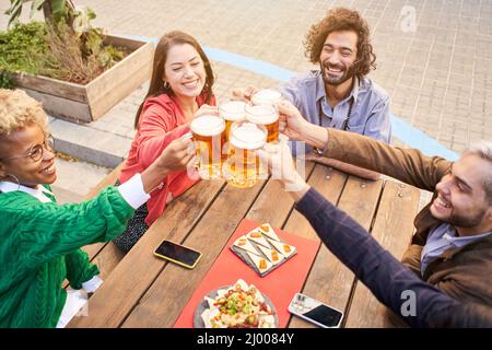 Gruppe attraktiver junger Menschen, die mit einem Bier toasten. Glückliche Freunde, die Spaß im Freien haben. Stockfoto