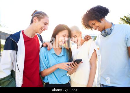 Gruppe o Freunde, die das Smartphone im Freien beobachten. Junge lächelnde Menschen teilen sich mit mobilen Zellen im Freien. Stockfoto