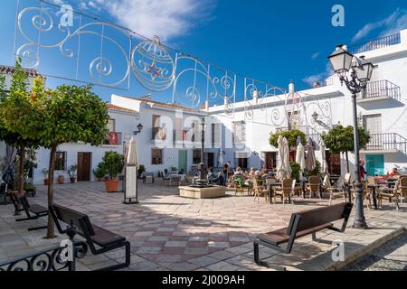 'Plaza de la Iglesia' - Kirchplatz im Zentrum des Dorfes Frigiliana. Menschen genießen einen sonnigen Wintertag im Januar Stockfoto