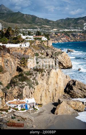 Panoramablick auf die schöne Stadt Nerja im Winter. Leerer 'Calahonda'-Strand. An einem windigen Tag plätschern Wellen. Wolkiger Himmel. Im Hintergrund Sierra Nevada Stockfoto