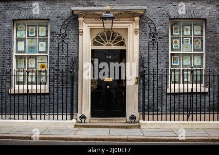 London, Großbritannien. 15.. März 2022.Bilder von Sonnenblumen, der Nationalblume der Ukraine, füllen die Fenster auf beiden Seiten der berühmten schwarzen Tür der Downing Street Nr. 10. Die Zeichnungen, die von Kindern aus dem ganzen Land entworfen wurden, werden in Solidarität mit dem ukrainischen Volk gezeigt. Chris Aubrey/Alamy Live News Stockfoto