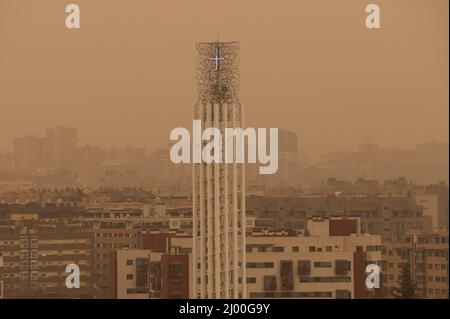 Madrid, Spanien. 15. März 2022. Der Turm einer Kirche wird mit Nebel gesehen, der durch eine große Menge von Staubpartikeln in Suspension aus der Sahara erzeugt wird, was zu einer Abnahme der Luftqualität, Sand in den Straßen, einem rötlichen Himmel und steigenden Temperaturen führt. Die Gemeinde Madrid hat empfohlen, wegen der schlechten Luftqualität die Aktivitäten im Freien zu beschränken. Quelle: Marcos del Mazo/Alamy Live News Stockfoto