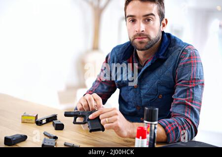 Regelmäßige Wartung ist für jeden Waffenbesitzer unerlässlich. Ein junger Mann, der seine Waffe putzt. Stockfoto