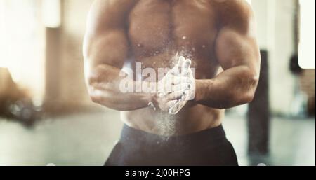 Hol dir den Griff. Ein kurzer Schuss eines unerkennbaren jungen Mannes, der während eines Trainings im Fitnessstudio seine Hände pudert. Stockfoto