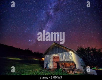 Blick auf den Sternenhimmel und das alte Haus am Berghang. Dramatische und malerische Szene. Ort Ort Karpaten, Ukraine, Europa. Entdecken Sie die Welt Stockfoto