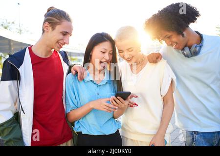 Gruppe multirassische junge Menschen mit mobilen Smartphone im Freien, sie schauen auf etwas mit einem überraschenden Gesicht. Mehrere ethnische Millennials Stockfoto