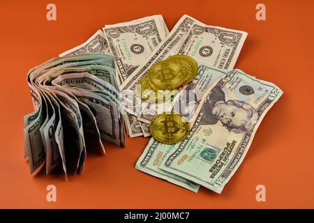 Gebrauchte und gerollte Bitcoin- und Dollarscheine, die auf einem orangefarbenen Hintergrund liegen. Stockfoto