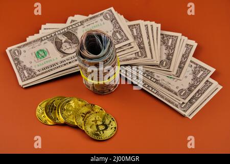 Gebrauchte und gerollte Bitcoin- und Dollarscheine, die auf einem orangefarbenen Hintergrund liegen Stockfoto