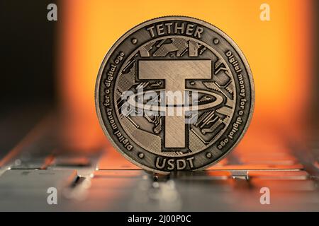 Tether USDT Cryptocurrency Physical Coin placed on Laptop Keyboard and lit with orange light from behind. Stockfoto