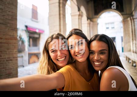 Drei glückliche Freundinnen, die zusammen Spaß haben und lächelndes Selfie machen Stockfoto