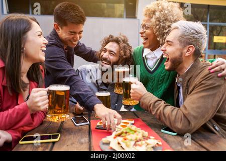 Eine Gruppe von Freunden genießt abends Getränke und Essen in der Bar. Fröhliche Menschen, die lachen Stockfoto