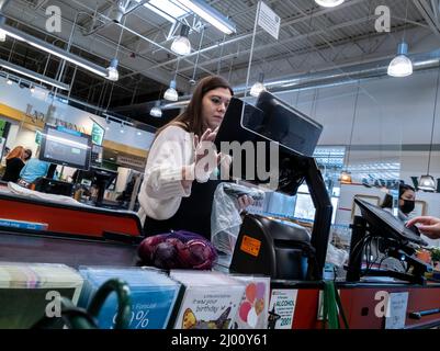 Lynnwood, WA USA - ca. März 2022: Niedrige schräge Ansicht eines Kassierers von Whole Foods ohne Maske, der einen Kunden hinter einem Plexiglasteiler auscheckt. Stockfoto