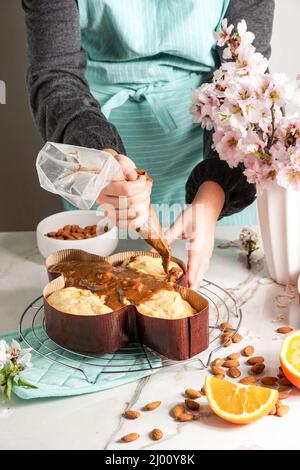 Colomba - traditionelle italienische easter Dove Kuchen, Prozess der Dekoration mit Haselnussglasur, Makaranage, bestreut mit Mandeln, Frau Schaffhand Stockfoto