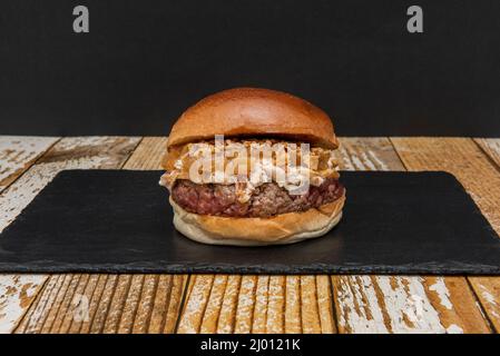 Großartiger Rinderburger mit karamellisierten Zwiebeln und knuspriger Zwiebel mit Spiegelei und geröstetem Brot auf einem Holzteller Stockfoto