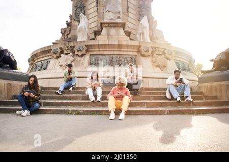 Süchtig Gruppe von Freunden mit ihren Smartphones. Individualistische Menschen konzentrierten sich auf ihre Handys, die auf einer Treppe in einer Stadt saßen. Technologie und Stockfoto