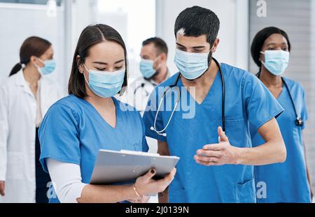 Besprechen, was als Nächstes zu tun ist. Aufnahme von zwei Ärzten, die in einem geschäftigen Krankenhaus Notizen durchgingen. Stockfoto