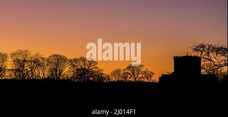 Panoramablick auf einen orangefarbenen Sonnenuntergang und die Silhouetten des Baumes und eines Gebäudes Stockfoto