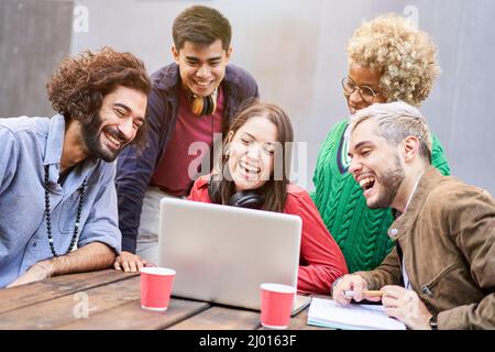 Eine Gruppe junger Studenten, die sich ein Video auf dem Laptop im Freien ansehen. Millennial lächelnde Menschen mit Laptop für Videoanruf Stockfoto