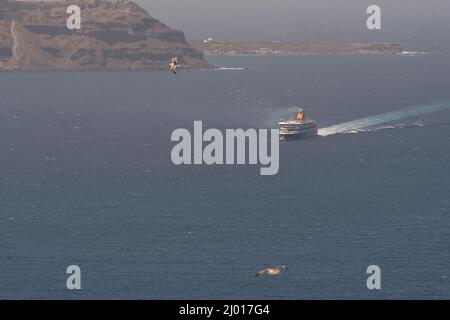 Santorini, Griechenland - 10. Mai 2021 - Eine Fähre nähert sich dem Hafen von Athinios in Santorini und Möwen fliegen herum Stockfoto