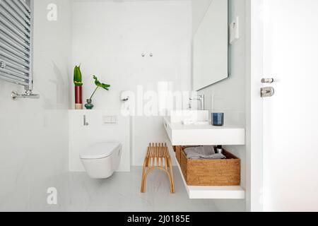 Badezimmer mit weißen Porzellanarmaturen, weiß gefliesten Wänden, Marmorfußboden und Hängeschränken Stockfoto