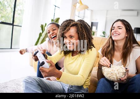 Wettbewerb multirassische junge Mädchen Freunde spielen Videospiele zusammen zu Hause. Nur Frauen spielen und essen Popcorn. Stockfoto