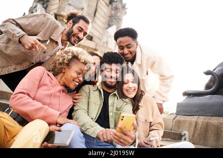 Guy zeigt seinen multirassischen Freunden ein Video auf dem Smartphone. Gruppe von Personen, die sich etwas auf einem Mobilgerät oder einem Smart-Gerät ansehen. Stockfoto