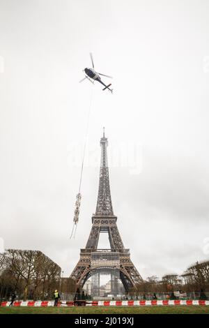 Paris, Frankreich. 15. März 2022. Ein Hubschrauber hebt am 15. März 2022 eine neue Antenne auf den Eiffelturm in Paris, Frankreich. Der Eiffelturm wuchs am Dienstag um sechs Meter, nachdem auf dem Pariser Denkmal eine neue Radioantenne installiert wurde, auf eine Höhe von 330 Metern. Quelle: Florent Michel/Xinhua/Alamy Live News Stockfoto