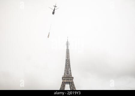 Paris, Frankreich. 15. März 2022. Ein Hubschrauber hebt am 15. März 2022 eine neue Antenne auf den Eiffelturm in Paris, Frankreich. Der Eiffelturm wuchs am Dienstag um sechs Meter, nachdem auf dem Pariser Denkmal eine neue Radioantenne installiert wurde, auf eine Höhe von 330 Metern. Quelle: Florent Michel/Xinhua/Alamy Live News Stockfoto