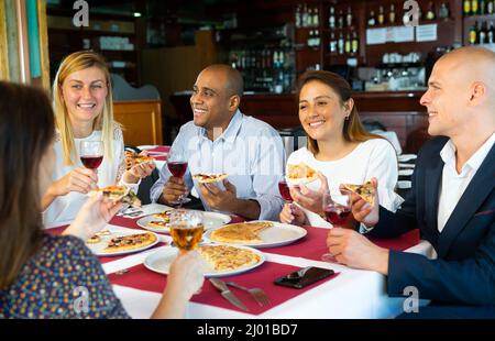 Fröhliche junge Erwachsene genießen Pizza im gemütlichen Restaurant Stockfoto