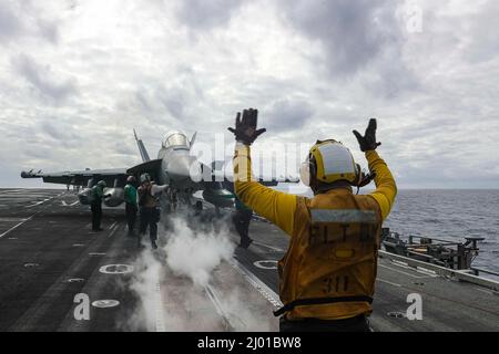 Philippine Sea, Vereinigte Staaten. 09. März 2022. U.S. Navy Aviation Boatswains Mate 1. Class Christopher Farrell, leitet einen EA-18G Growler Kampfjet, der an den Wizards of Electronic Attack Squadron 133 befestigt ist, für den Start vom Flugdeck des Nimitz-Klasse Flugzeugträgers USS Abraham Lincoln während des Routinebetriebs am 9. März 2022 in der philippinischen See. Kredit: MC3 Javier Reyes/Planetpix/Alamy Live Nachrichten Stockfoto