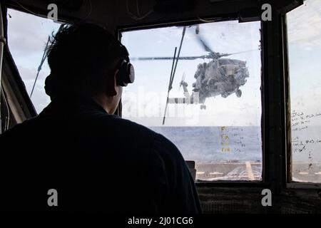 PHILIPPINISCHES MEER (14. März 2022) LT. j.g. Jian Miclat aus Chula Vista, Kalifornien, fungiert als Hubschrauber-Kontrolloffizier und koordiniert mit dem Offizier der Brücke und des Landezeichens den Start eines MH-60R-Hubschraubers, der dem Helicopter Maritime Strike Squadron (HSM) 51 vom Deck des Arleigh Burke-Klasse-Lenkflugkörper-Zerstörers USS Dewey (DDG 105) zugewiesen wurde. Während der Durchführung von Routineoperationen im Zuständigkeitsbereich der US 7.-Flotte. Dewey wird Destroyer Squadron (DESRON) 15 zugewiesen und unterstützt derzeit einen freien und offenen Indo-Pacific. CTF 71/DESRON 15 ist die LAR der Marine Stockfoto