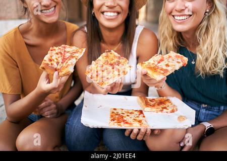 Nahaufnahme der Pizza. Drei schöne Frauen sitzen auf den Treppen der Straßen der Stadt essen Street Food. Die glücklichen Mädchen genießen das Wochenende zusammen. Stockfoto