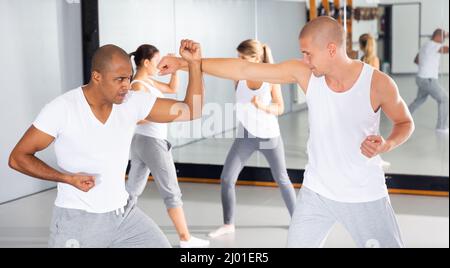 Männer üben grundlegende Bewegungen während des Selbstverteidigungskurses im Fitnessstudio Stockfoto